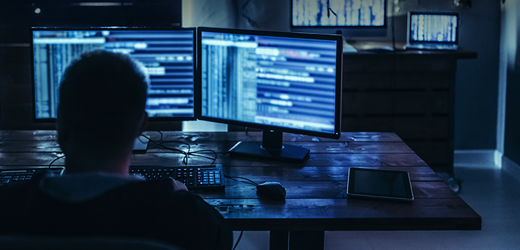 Man on multiple computers in dark room 