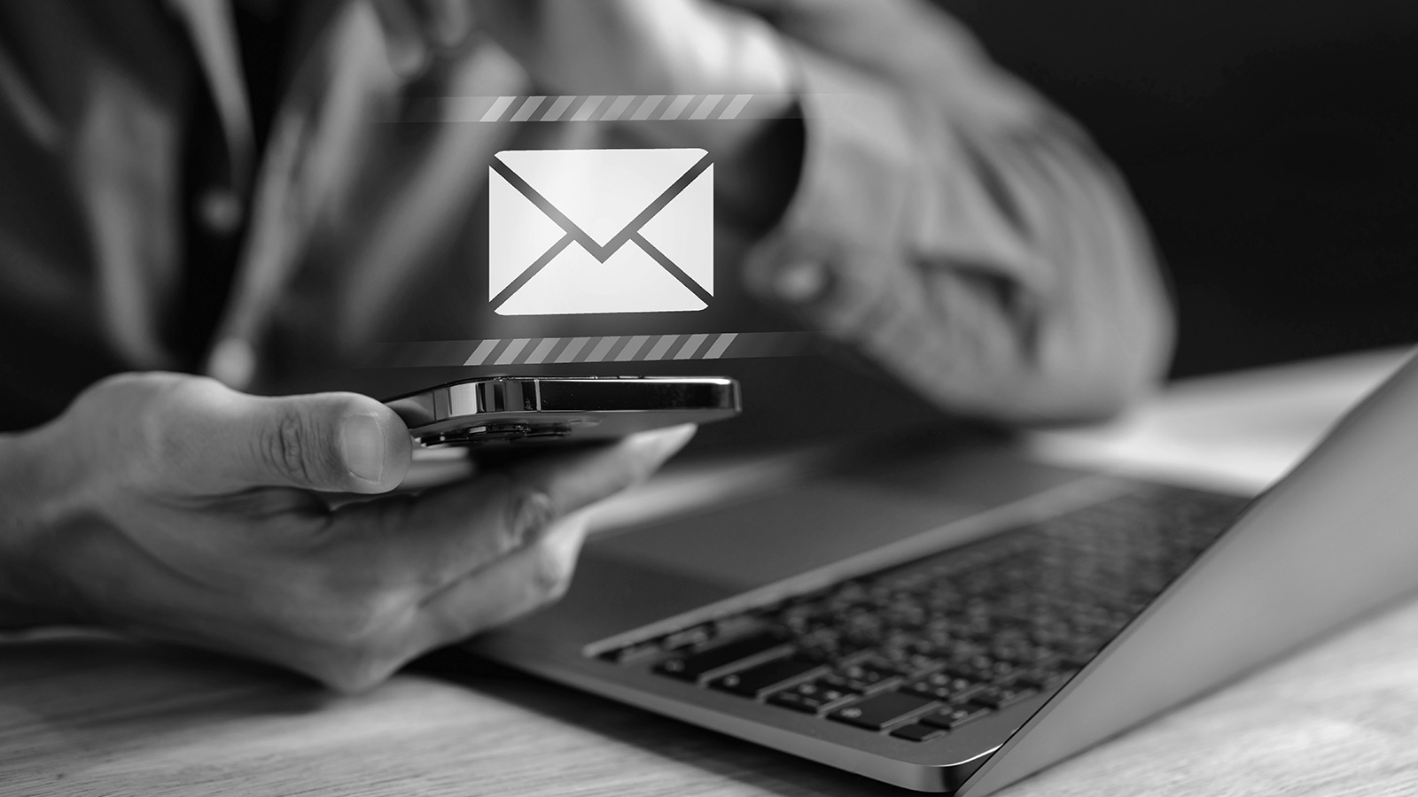 man checking email on phone in front of laptop