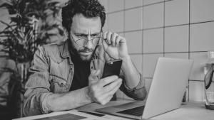 man in front of laptop looking at mobile phone